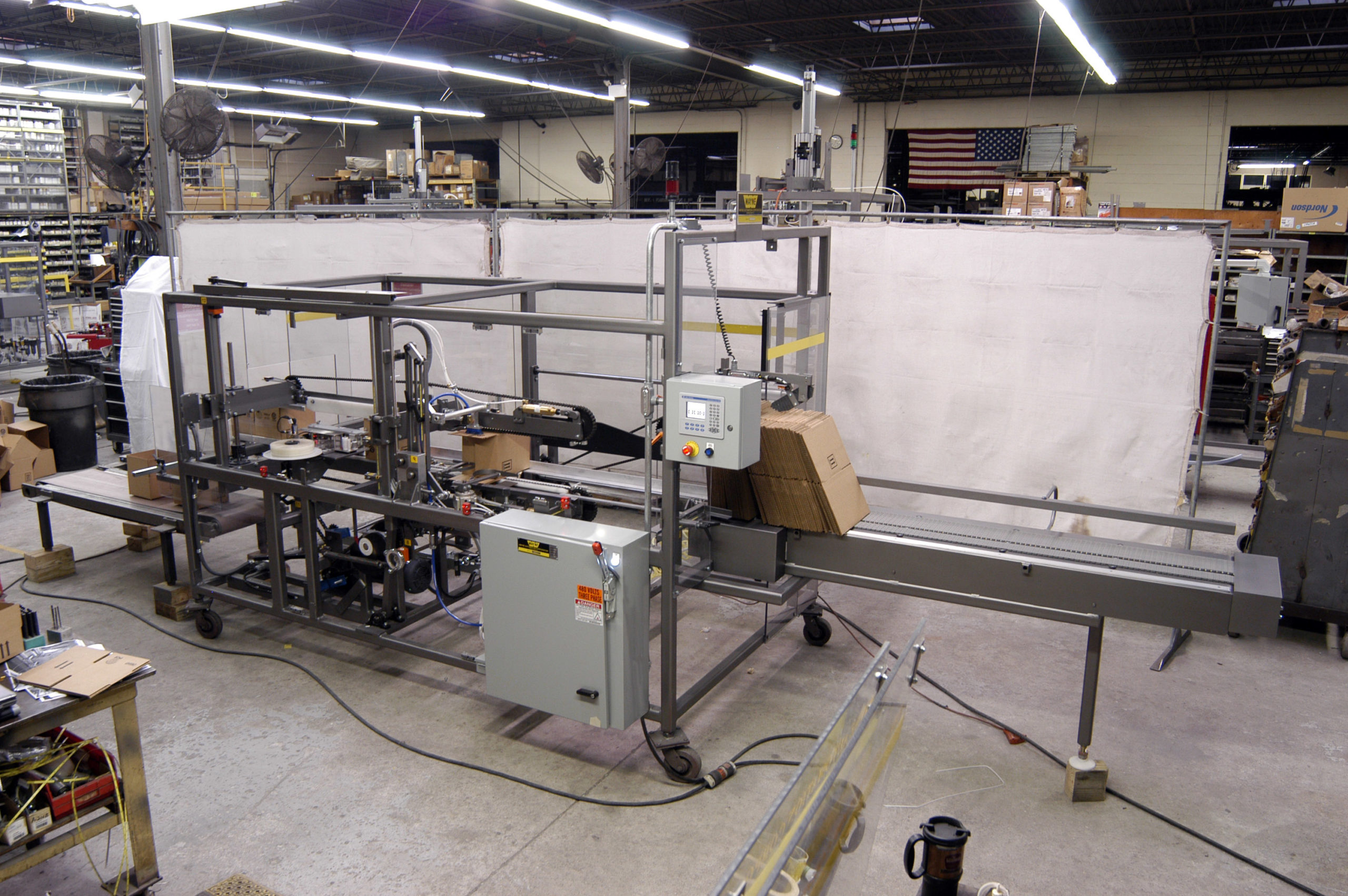 Large case erector from Wayne Automation sits on warehouse floor, assembling a high volume of corrugated boxes. 