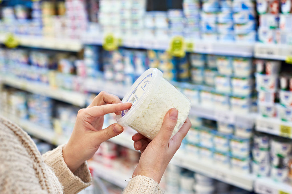 Buyer hands with plastic container of cottage cheese in the grocery store