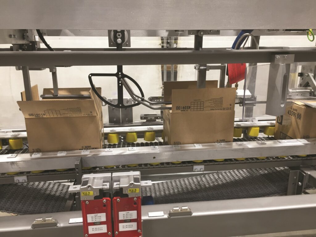 Cardboard boxes on a conveyor belt of Wayne Automation’s RPS-LR Case Sealer machine.