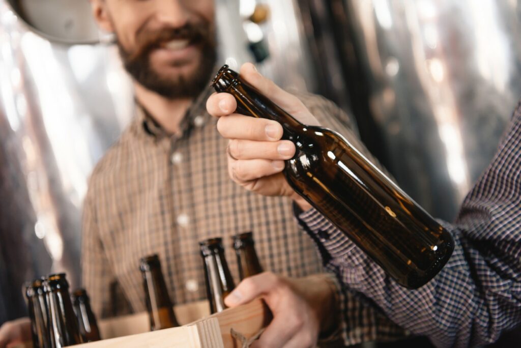 A person holds a carton of empty brown beer bottles while another person holds one.