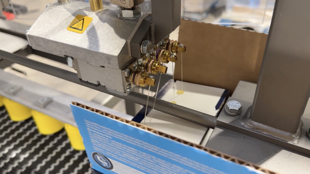 Automated case sealer applying tape to a closed box on a conveyor line in a packaging system. 