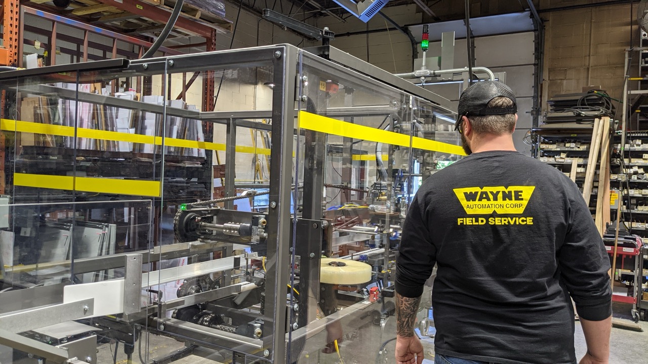 Wayne Automation field service technician performing maintenance on a case erector inside a manufacturing facility.